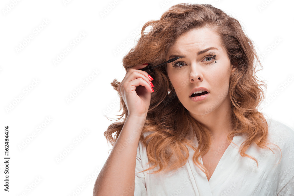 confused woman looking at camera while applying mascara isolated on white confused woman looking at camera while applying mascara isolated on white