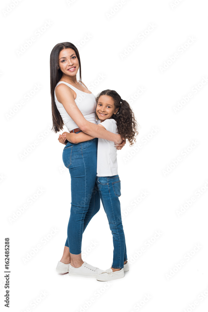 mother and daughter looking at camera while hugging each other isolated on white