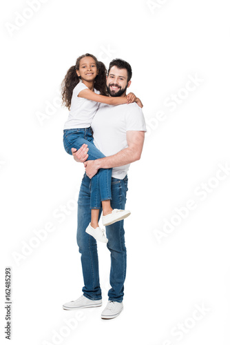 Happy father carrying adorable little daughter and smiling at camera