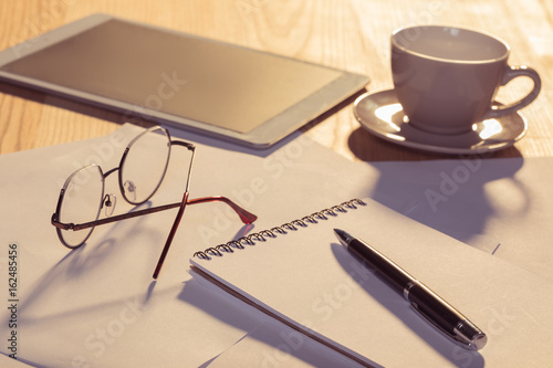 Close-up view of digital tablet with eyeglasses, cup of coffee and papers on table