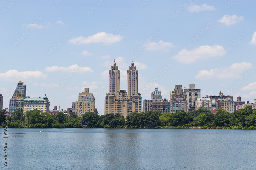 High resolution panorama of Central Park West skyline and the Jacqueline Kennedy Reservoir in New York City with apartment skyscrapers over lake with fountain in midtown Manhattan and lake reflection