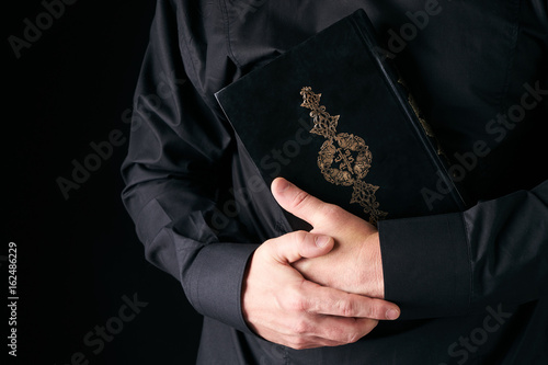 Holy Koran/Quran in Man's hand - holy book of Muslims. Black background with copy space . Public item of all muslims