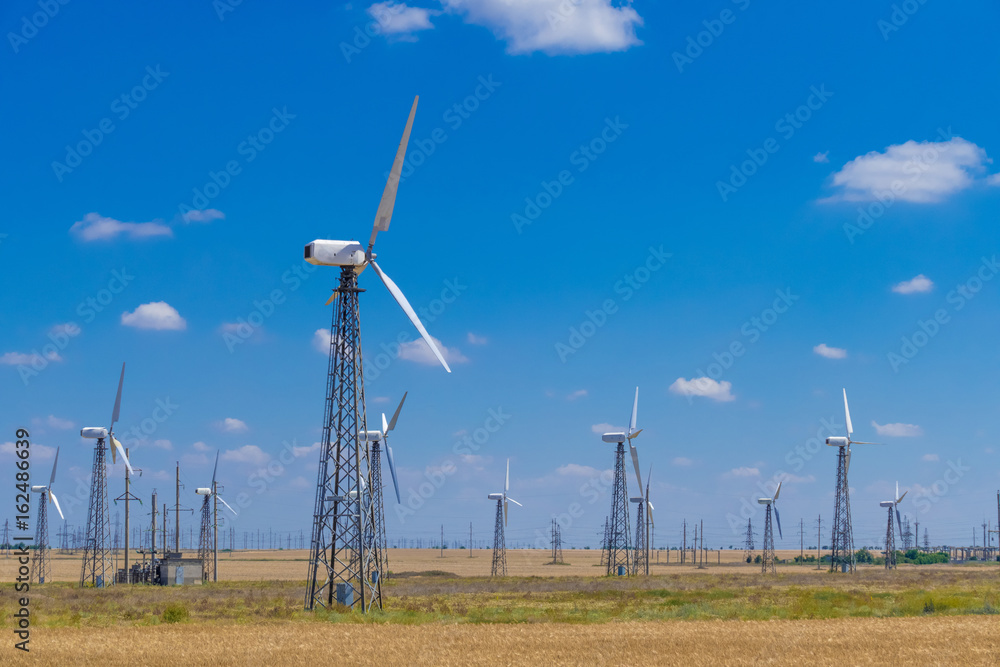 Wind turbines in wheat field / Propellers of windmills on blue sky background, close-up Wind turbines in wheat field / Propellers of windmills on blue sky background, close-up