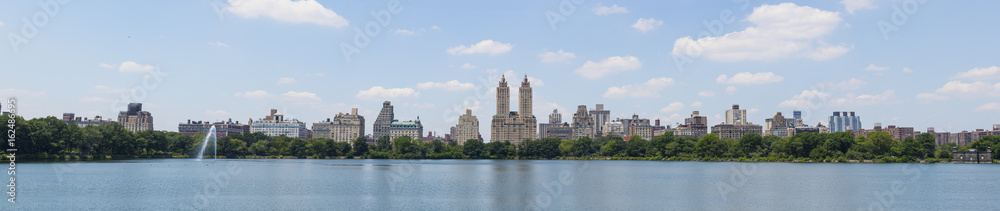 High resolution panorama of Central Park West skyline and the Jacqueline Kennedy Reservoir in New York City with apartment skyscrapers over lake with fountain in midtown Manhattan and lake reflection