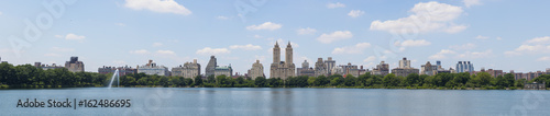 High resolution panorama of Central Park West skyline and the Jacqueline Kennedy Reservoir in New York City with apartment skyscrapers over lake with fountain in midtown Manhattan and lake reflection