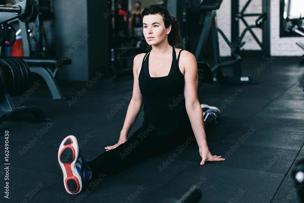 Fitness sportswoman in fashion sportswear doing twine and sitting on the floor in the gym. Sports clothing and shoes, urban style.