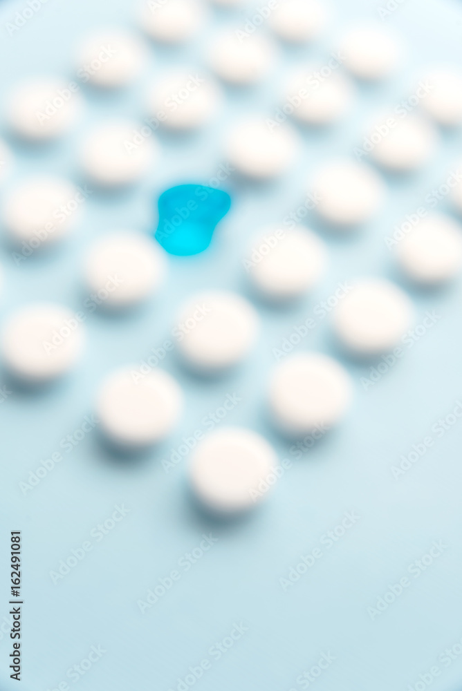 One blue liquid capsule in a grid of white tablets