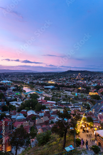 Sunset view of Tbilisi, capital of Georgia country, from Narikala fortress. Metekhi church, Holy Trinity Cathedral (Sameba), Presidential Administration, Bridge of Peace with illumination.
