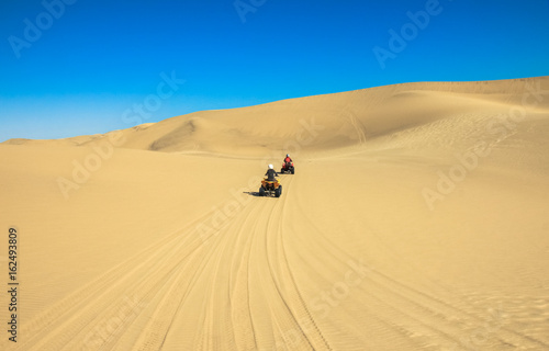 Quad driving people - two happy bikers in sand desert.