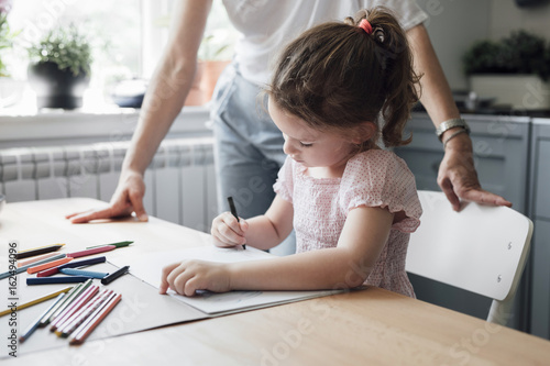 Cute little Caucasian girl drawing with crayons on kitchen table. photo