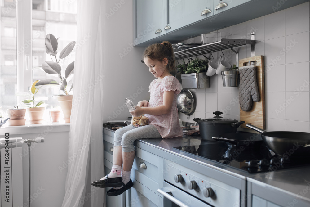 Girl sitting on kitchen table holding jar with cookies Girl sitting on kitchen table holding jar with cookies