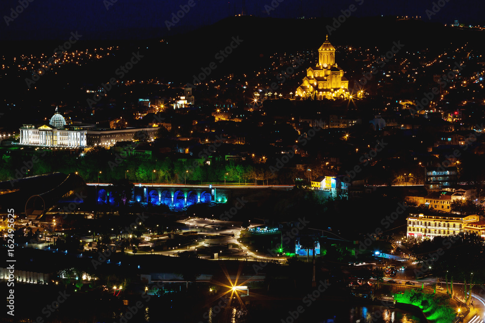Night panorama view of Tbilisi, capital of Georgia country. Holy Trinity Cathedral (Sameba) and Presidential Administration at night with illumination and moving cars.
