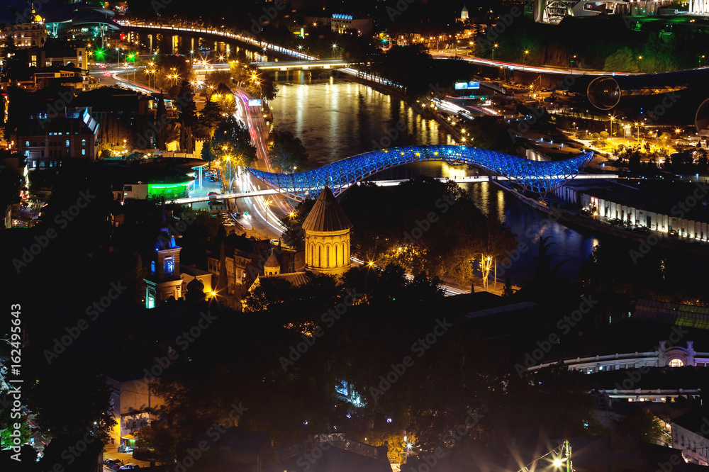 Night aerial view on illuminated Bridge of Peace over Kura river. Famous landmark in Tbilisi, Georgia.