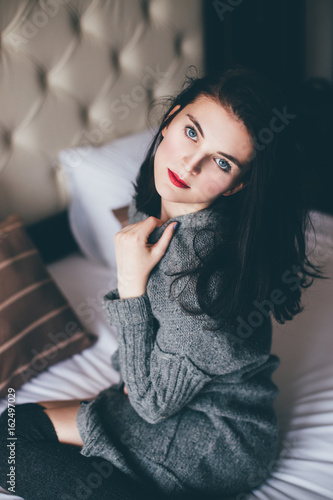 Young beautiful woman in a grey sweater and socks posing in a cozy bedroom