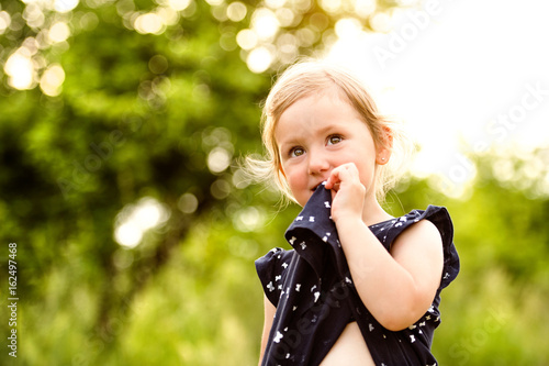 Cute little girl outside in in green sunny summer nature.