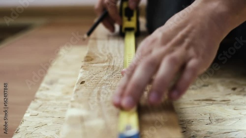 Male carpenter measuring wooden bar with ruler and marking it. DIY and handicraft concept.  