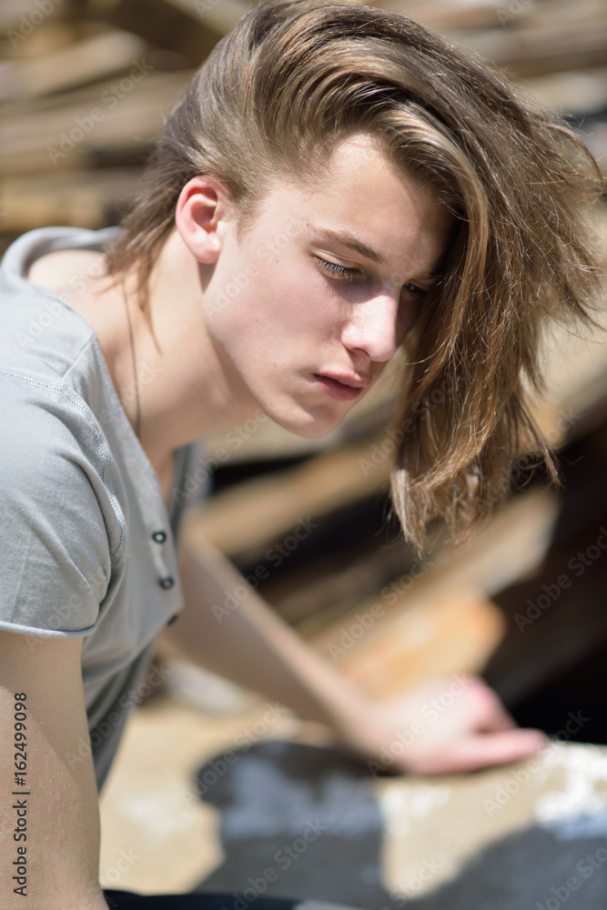 Portrait of young handsome man over wood boards, outdoor. Attractive trendy fashion 18 years old teen boy posing outside over construction waste Portrait of young handsome man over wood boards, outdoor. Attractive trendy fashion 18 years old teen boy posing outside over construction waste