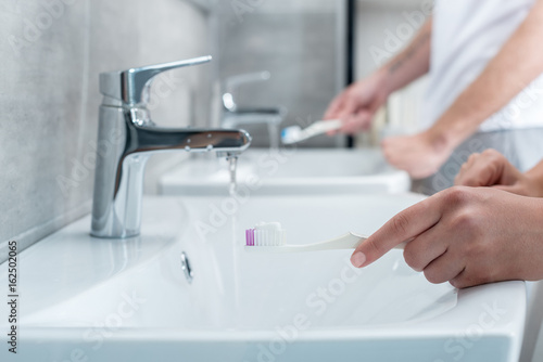 cropped view of couple brushing teeth at washbasin in bathroom, morning routine concept