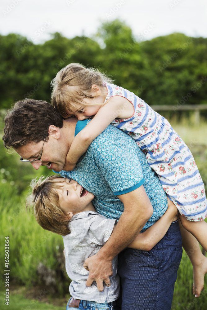 A father and two children in a garden, a boy hugging him around the waist and a girl on his back with arms around his neck. A father and two children in a garden, a boy hugging him around the waist and a girl on his back with arms around his neck.