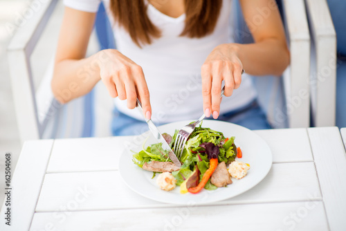 Break for energy, vitamins and refreshness. Close up cropped photo of lady, eating salad on a white modern wood table in an open air restaurant photo