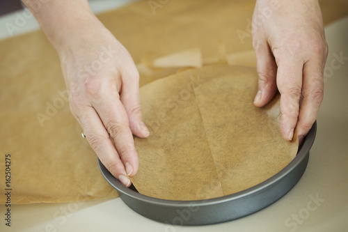 Close up of a cook, a cake maker lining the bottom of a round baking tin with baking paper.