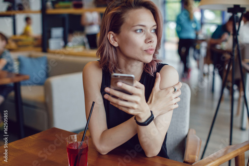 Attractive woman using smartphone and drinking a cocktail in a cafe.