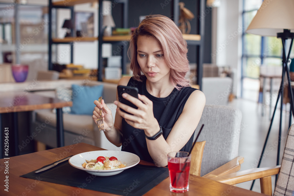 Attractive woman using smartphone and eating in a cafe.