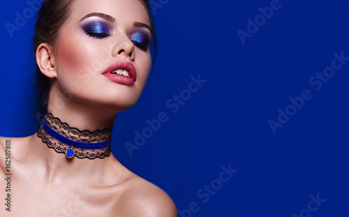 Beautiful young girl with flowing wavy hair and bright make-up. Blue shades of metallic, pink matte lipstick. Choker, lace, velvet, jewelry on the neck. Bijouterie, cosmetics, advertising. photo