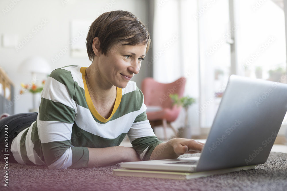 Smiling woman lying on the floor at home using laptop Smiling woman lying on the floor at home using laptop