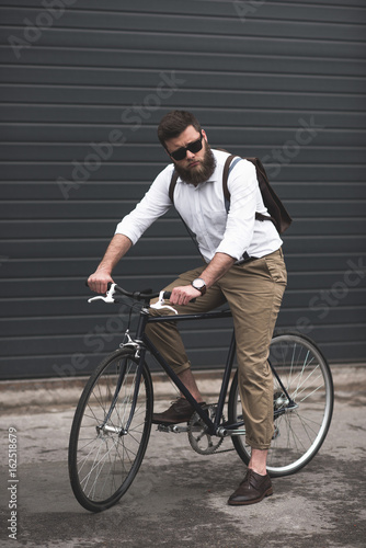 serious stylish young man in sunglasses riding bicycle