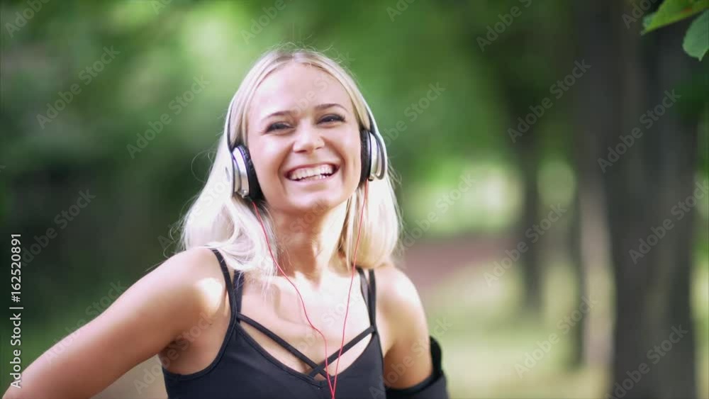 Portrait of a woman in headphones smiling against a background of green trees. Portrait of a woman in headphones smiling against a background of green trees.