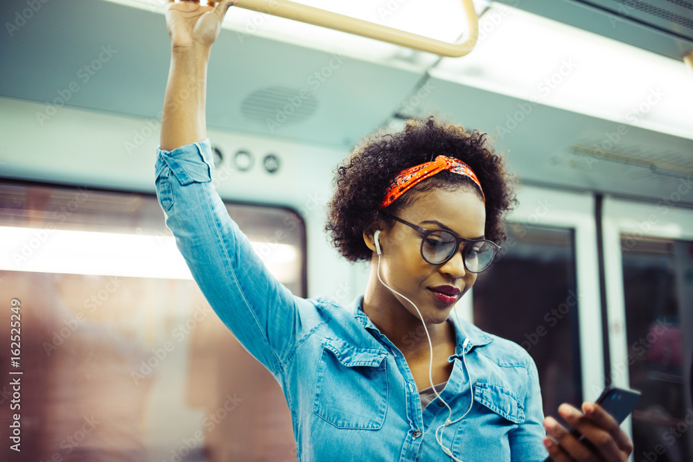Φωτογραφία Smiling young African woman listening to music on the subway
