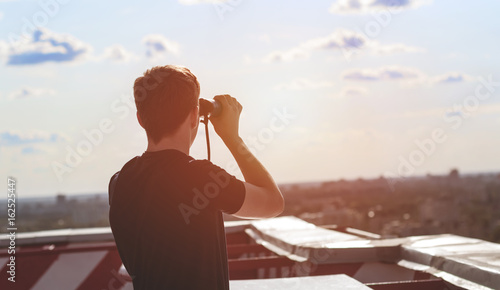 A young man with binoculars watching from the roof of the house