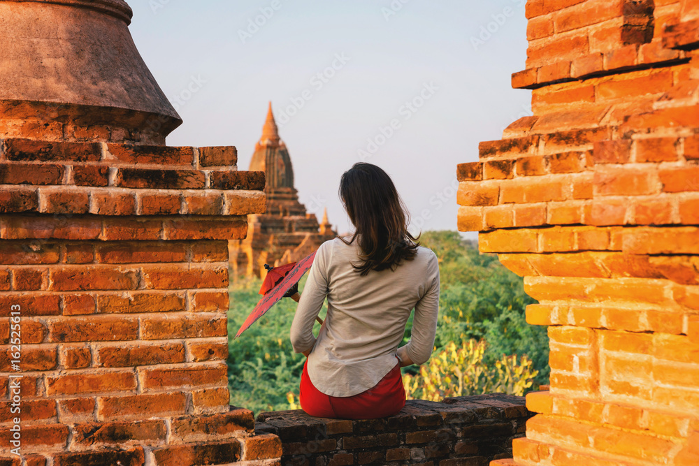 Girl enjoying a looking at Buddhist pagoda, Burma,Asia.A girl with a traditional Burmese umbrella relaxing in an ancient temple during sunset, Bagan,Myanmar.Ancient temples in Bagan in sunny sunset.