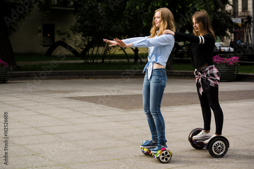 Two girls go on hoverboards one after another. Brunette and blonde on a hoverboard. photo