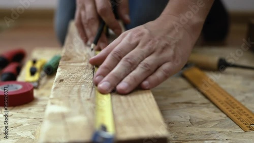 Close-up of constructor hands measuring lumber with tape on the floor. 