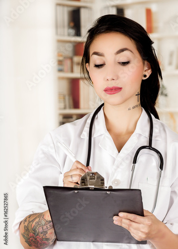 Beautiful tattooed young doctor in office background photo