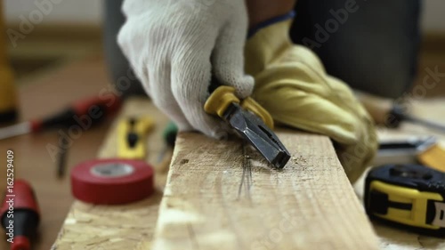 Professional carpenter using pliers while working with wooden board. 