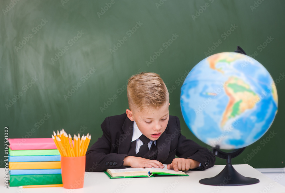 Young boy reading a book near empty green chalkboard Young boy reading a book near empty green chalkboard