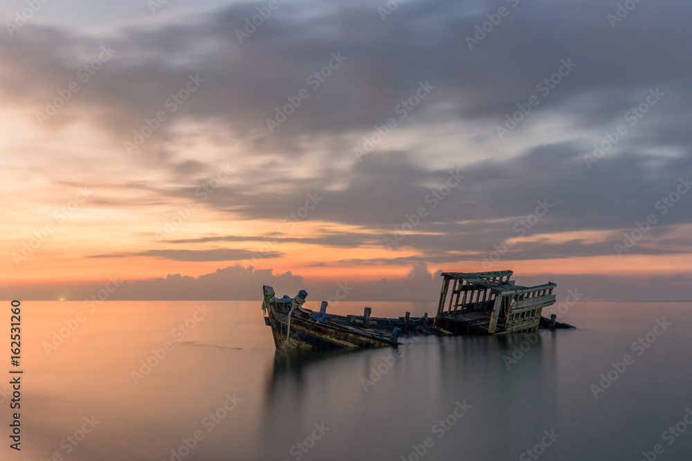 An old shipwreck or abandoned shipwreck taken during a beautiful sunset , Wrecked boat abandoned stand on beach or Shipwrecked off the coast of Thailand.