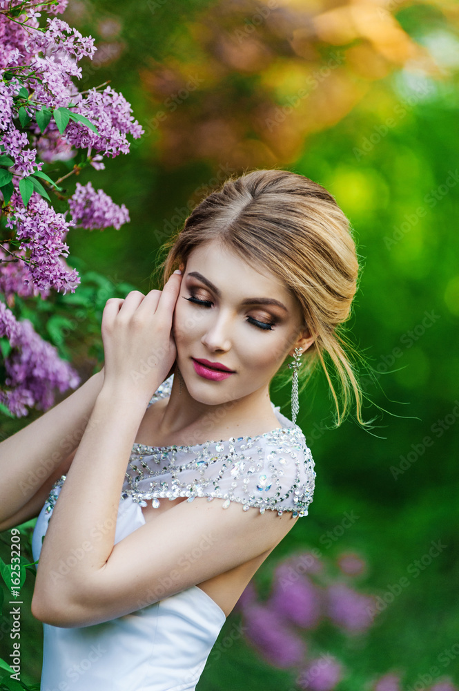 Elegant fashion model in a long white dress posing in the park Elegant fashion model in a long white dress posing in the park