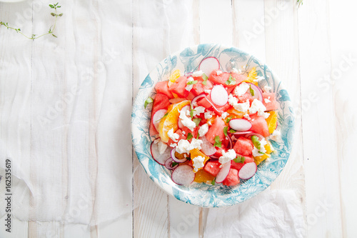 Watermelon salad with orange, radish and red onion on white distressed wooden table. Summer raw organic food concept. Flat lay with copy space.