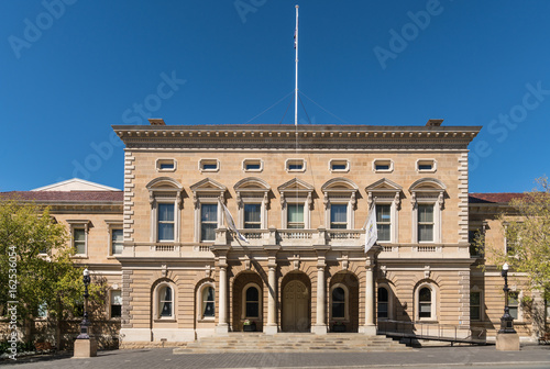 Hobart, Australia - March 19. 2017: Tasmania. The beige rectangular facade of historic Town Hall under blue sky. Some green trees on side. White flag mast on top.