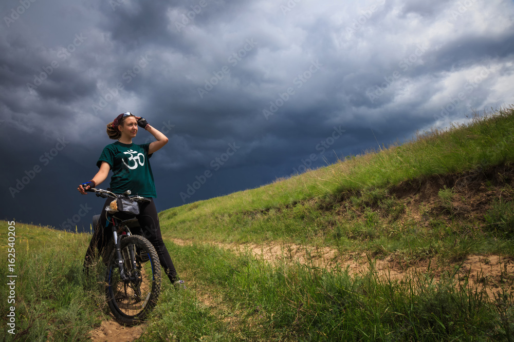 Young girl on a bike outdoors on the background of the thunderhead front