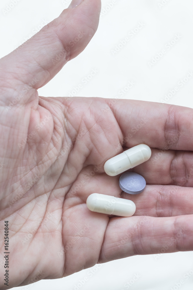 one hand holding white and purple pills, coated tablets, one hand holding white and purple pills, coated tablets,