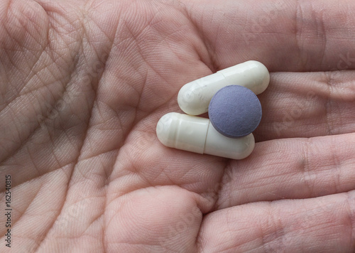 one hand holding white and purple pills, coated tablets,