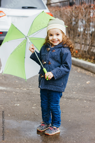 Little girl playting on the rainy street with green umbrella. photo