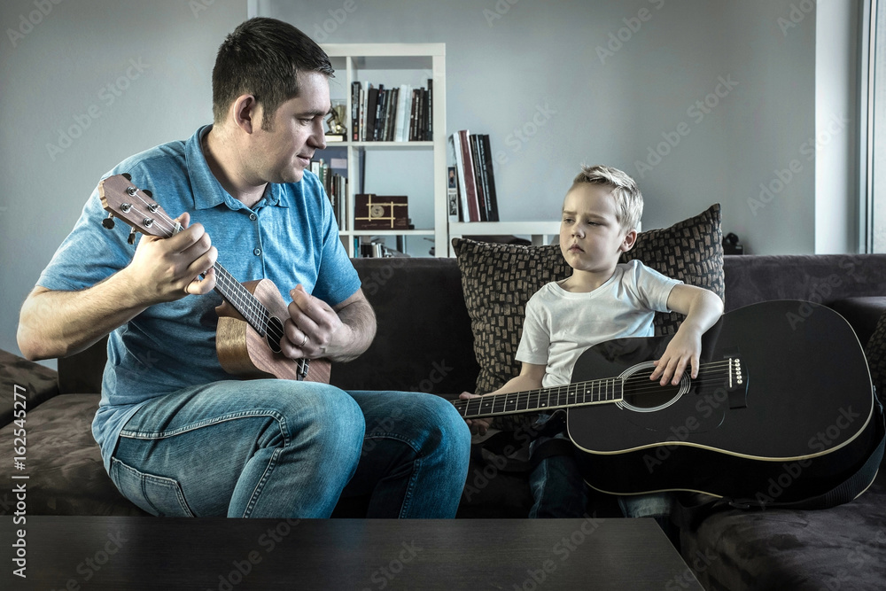 Father teaching his son to play on guitar at home. Son play on u
