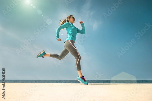 Woman running along the sealine coast under sunlight at sunny su