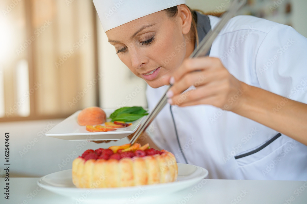 Pastry chef in professional kitchen decorating raspberry cake with fruits Pastry chef in professional kitchen decorating raspberry cake with fruits